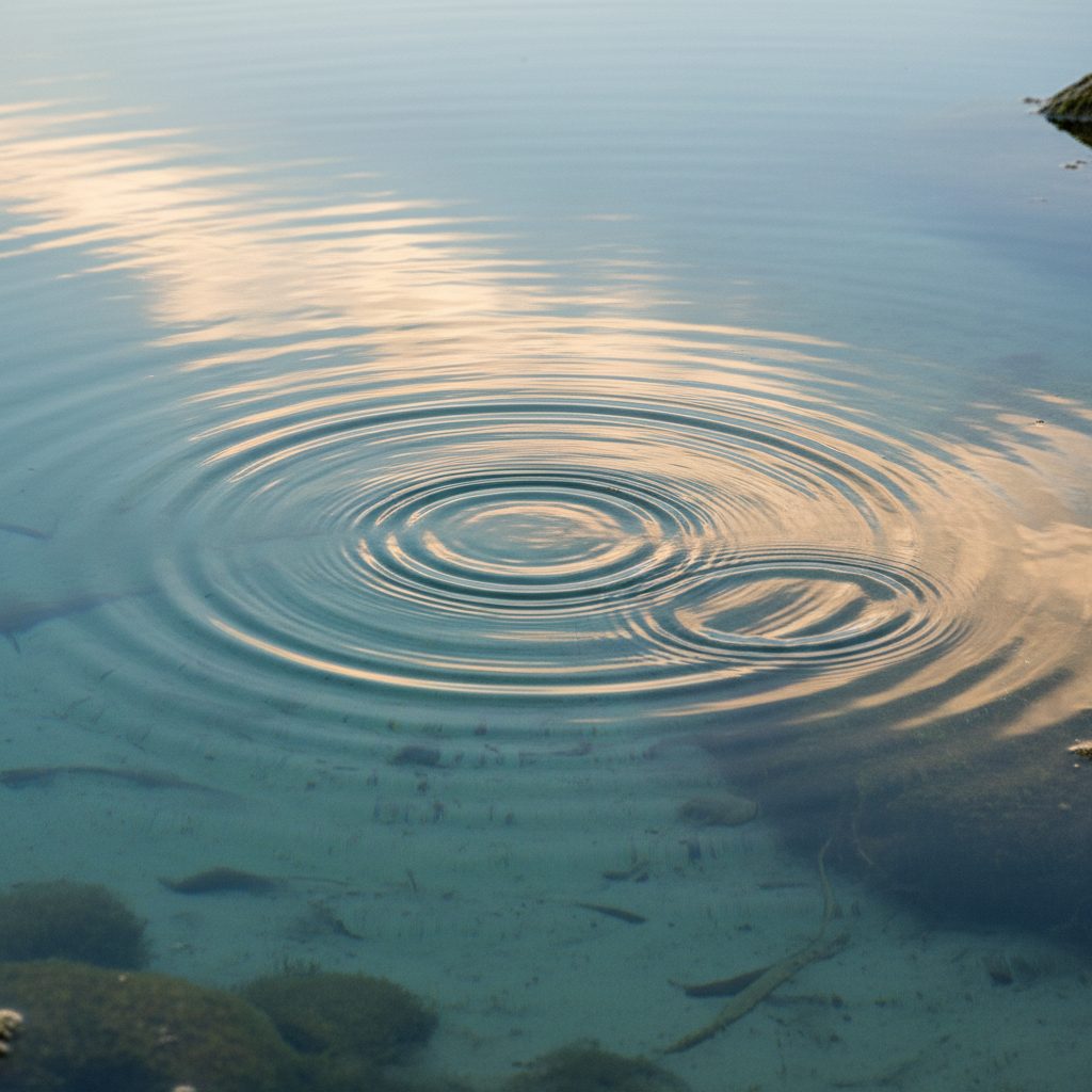 Ruhige Wasseroberfläche mit sanften Wasserkreisen über klarem, flachem Grund